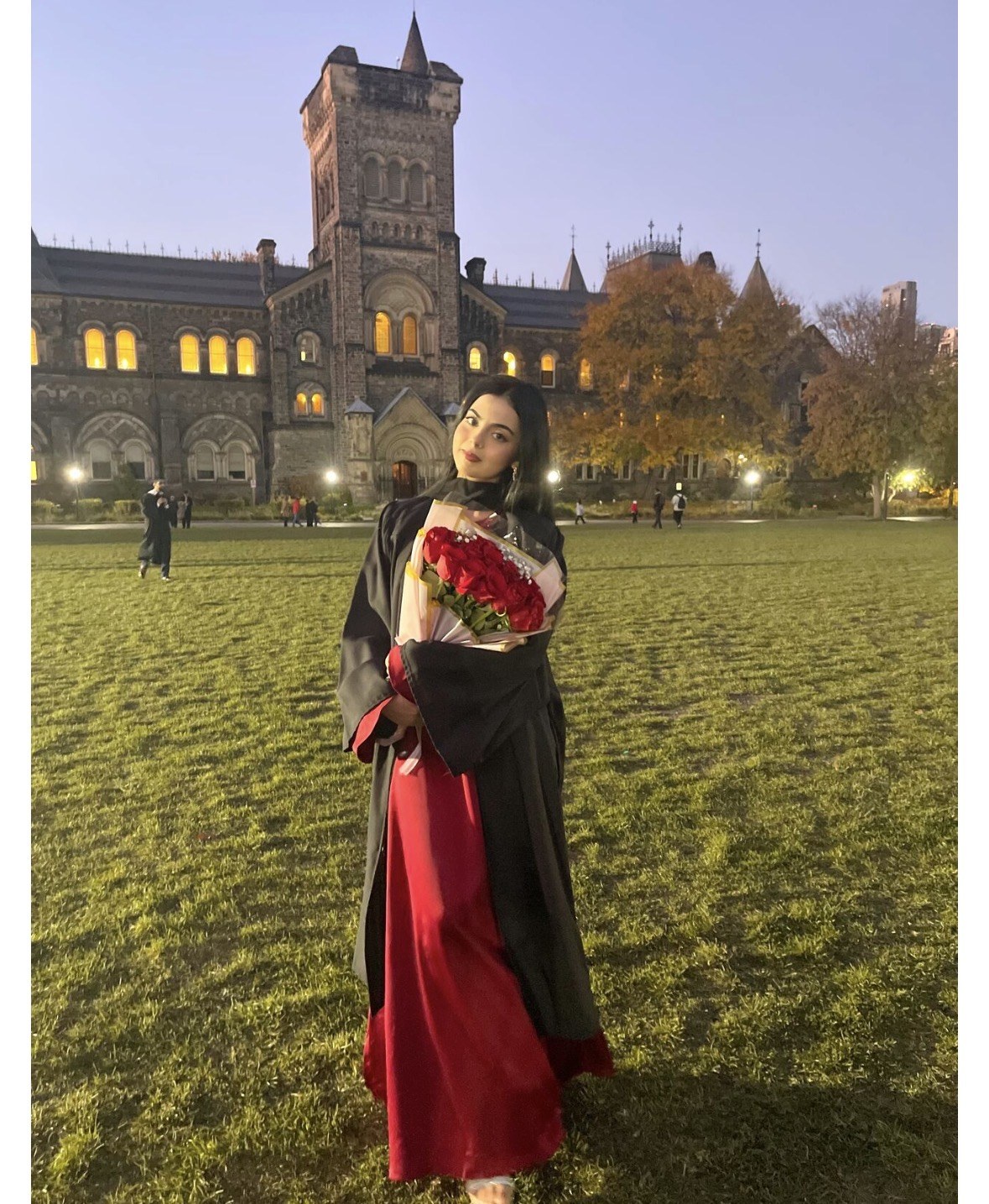 Nashrah Fatima at her graduation from the University of Toronto, holding a bouquet of red roses in front of University College